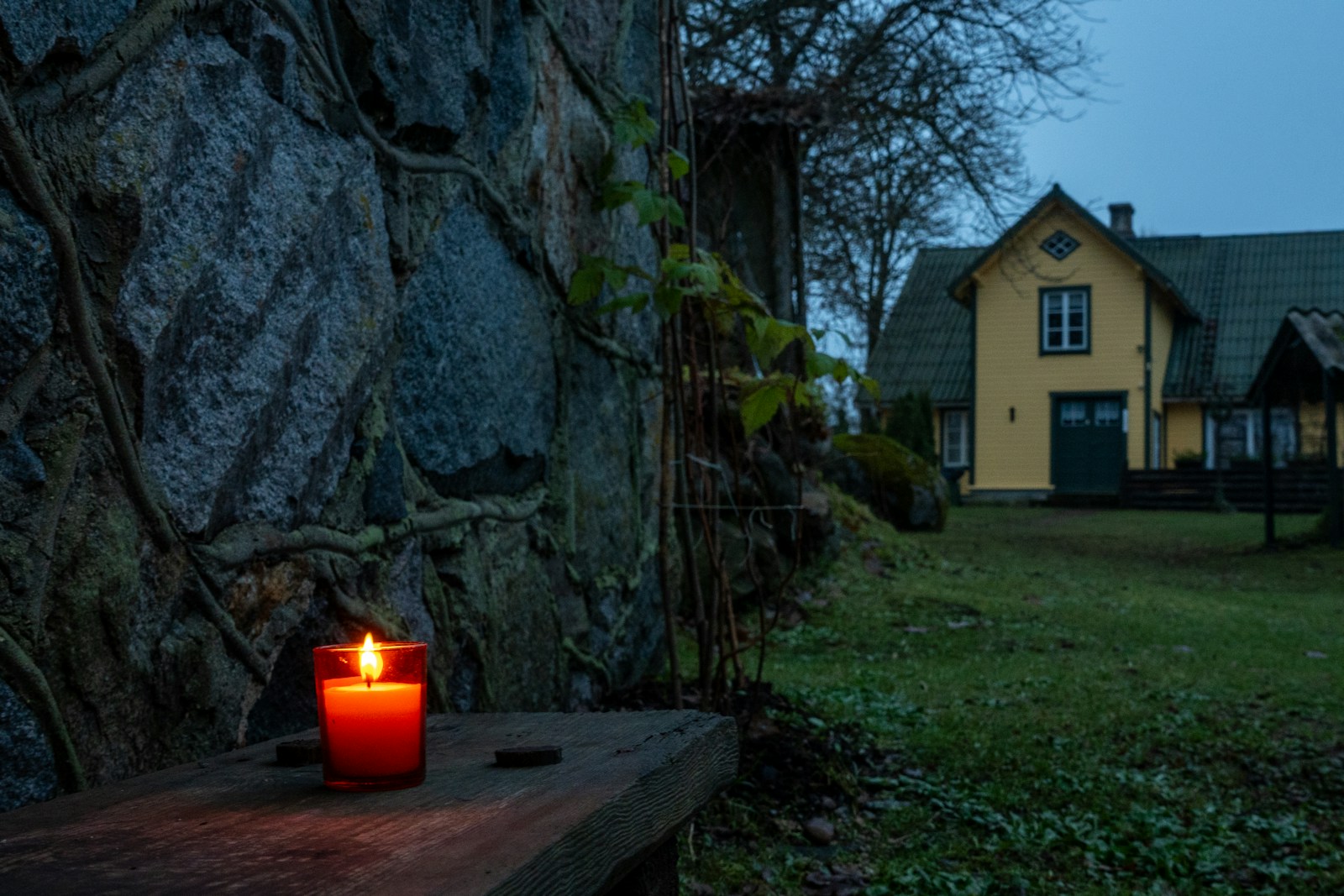 Candle lit on a wooden bench near a stone wall.
