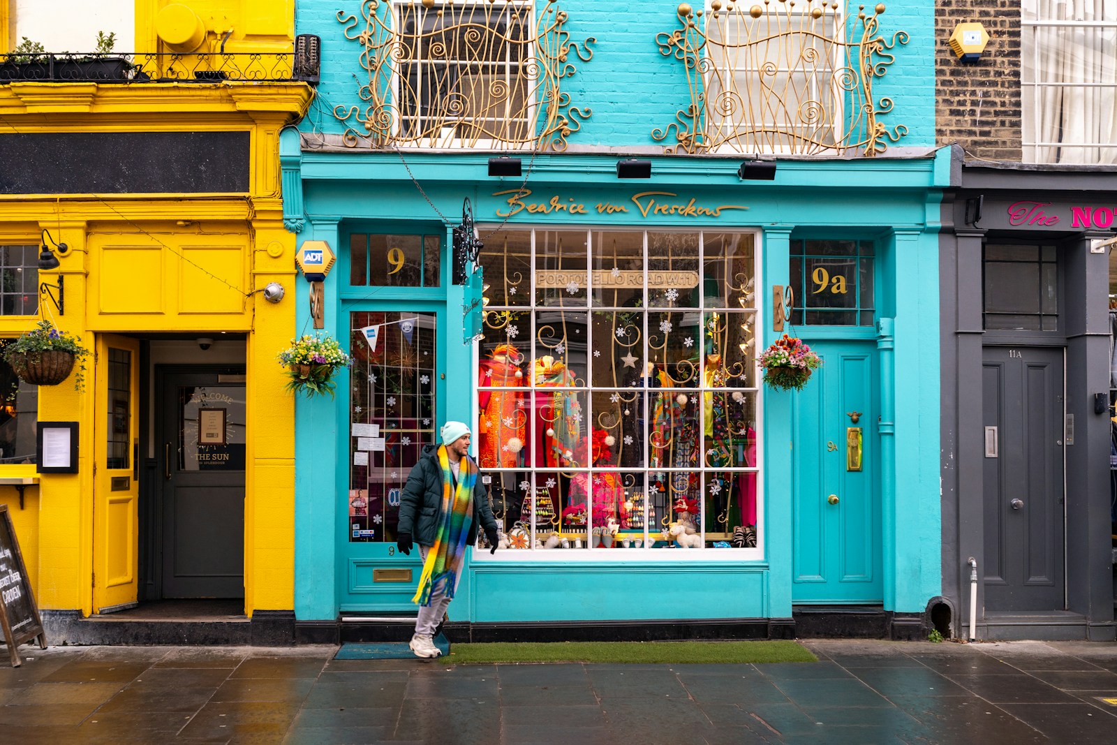 Person walks past colorful shops on a wet street.